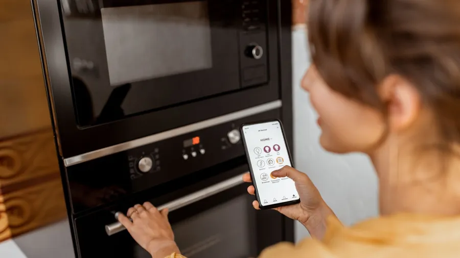 A woman controlling the oven with her smartphone.