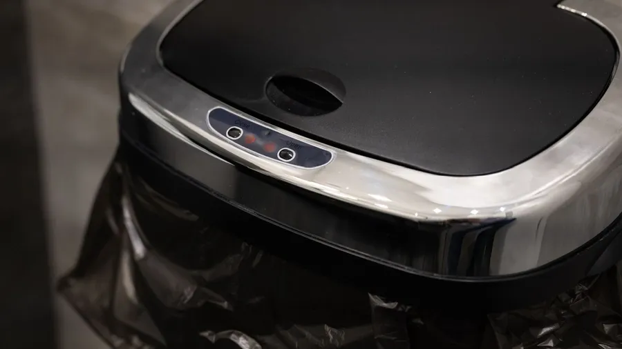 A black and silver smart trash can with a bin bag lined in it.