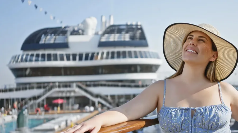 smiling woman in sunhat standing on cruise ship deck with