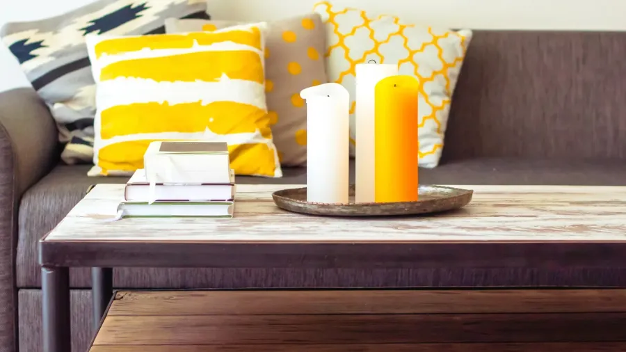 A wooden coffee table with stack of books and candles on a tray.