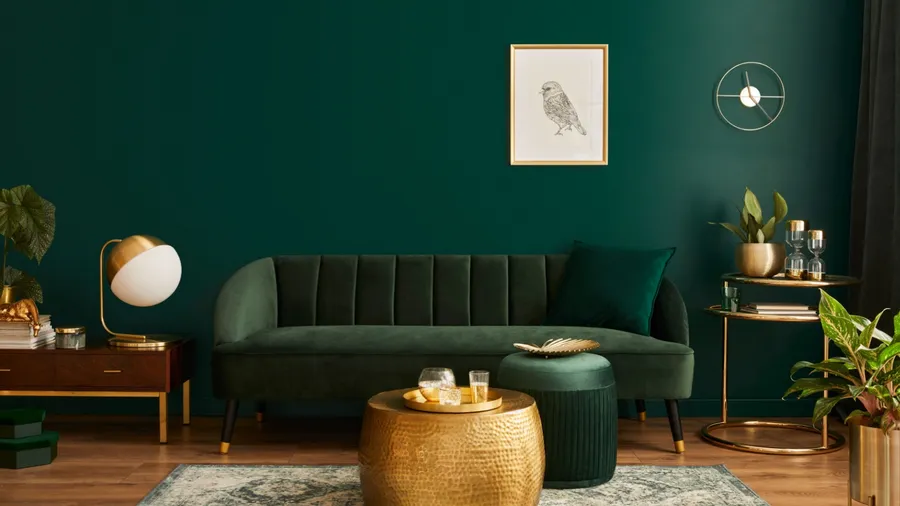 A stylish living room with a dark green color scheme, featuring a green velvet sofa, gold accents, and modern décor elements.