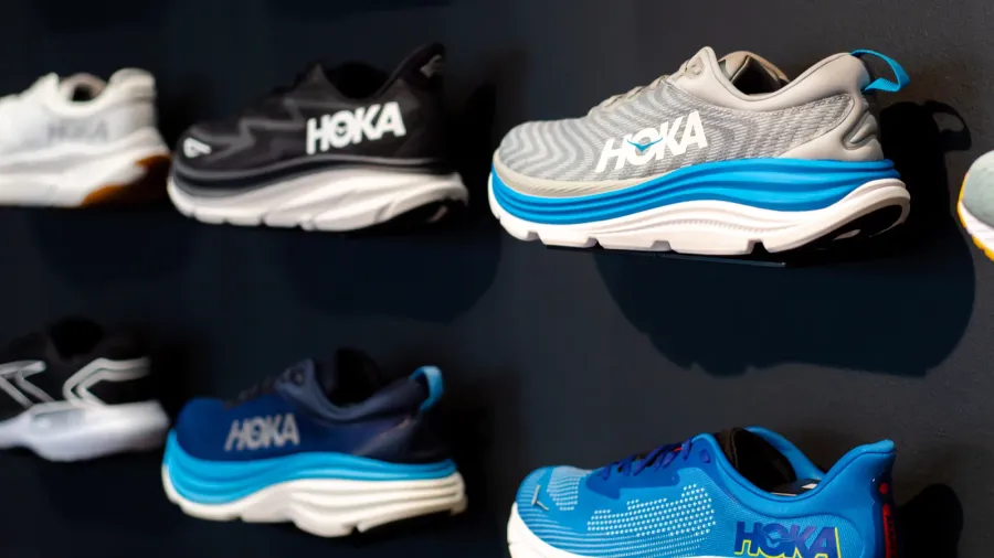 A display of various Hoka sneakers in different colors hanging on a black wall.