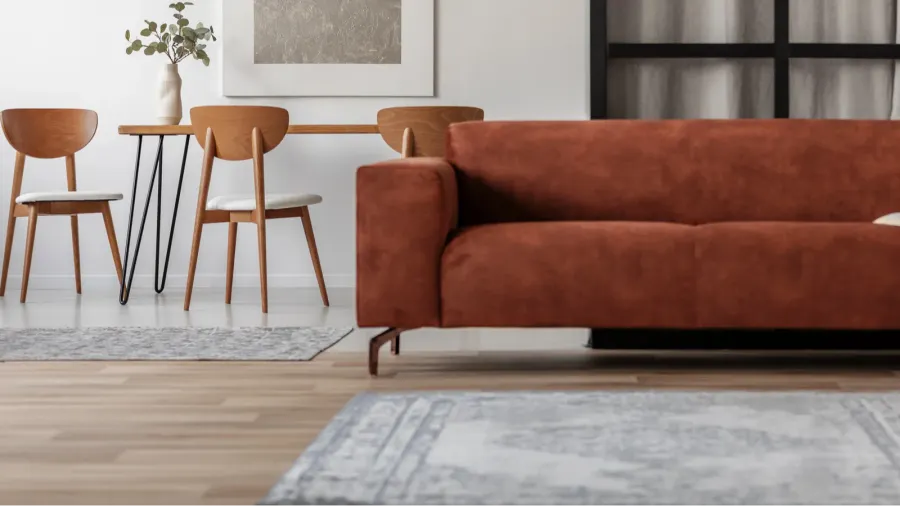 A contemporary living space showcasing a rich brown sofa, minimalist dining table and chairs, and a light area rug on wooden flooring.