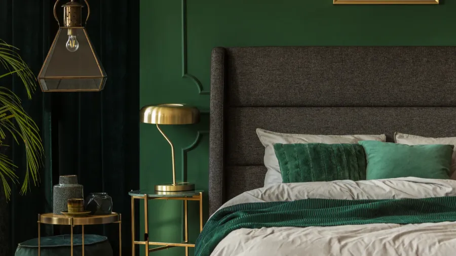 A contemporary bedroom with dark green walls, a gray upholstered headboard, and matching bedding and pillows.