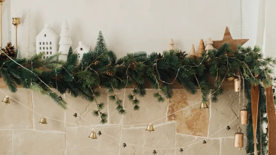 A fireplace decorated with Christmas tree branches, bells, and wooden accents.