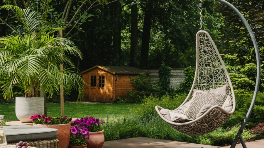 A beautiful garden with fancy egg chair, potted flowers in planters, and a garden shed in the background.
