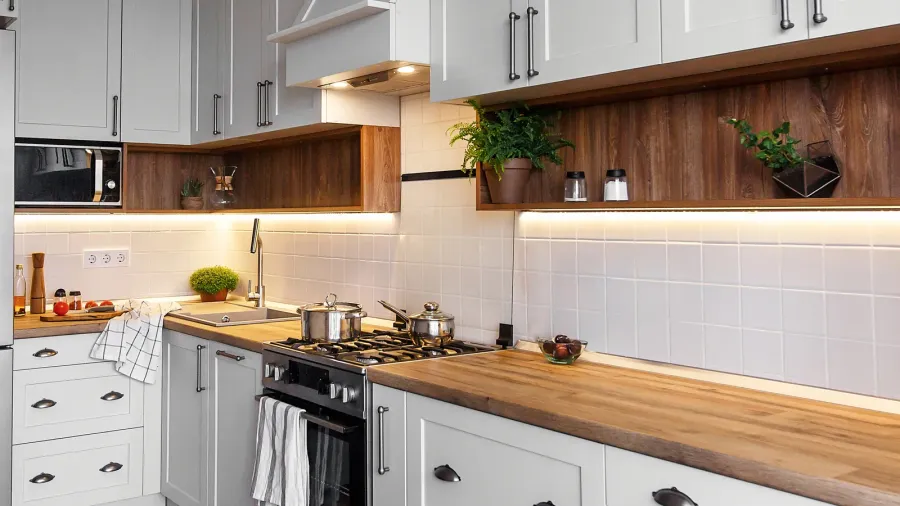 A modern kitchen features sleek gray cabinetry, wood accents, and bright lighting with pots on the stove.