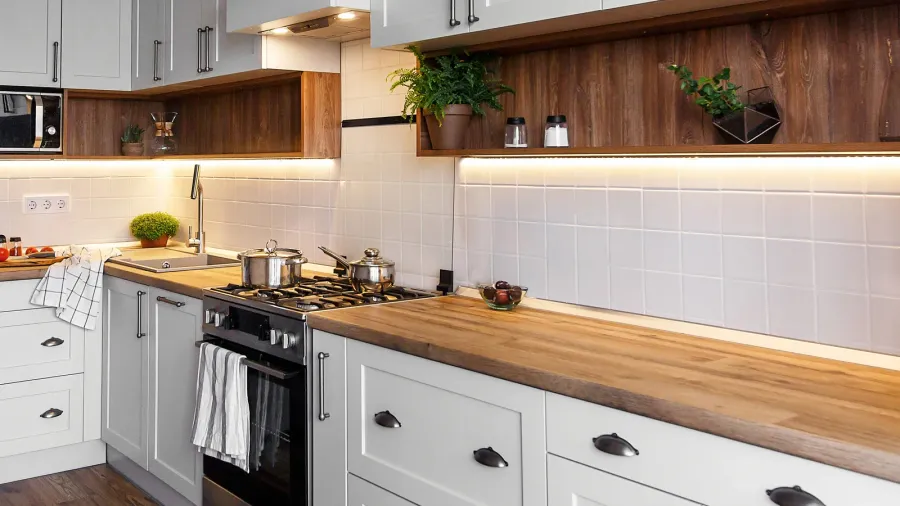 A stylish kitchen interior with modern cabinets, wooden countertop, dark wood open shelving, and stainless steel sink.