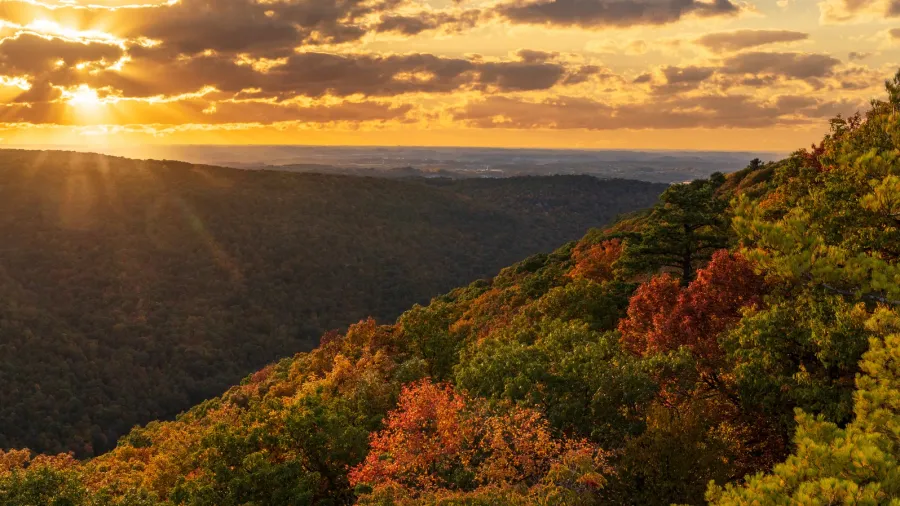 sun setting behind clouds illuminating the fall colors of the