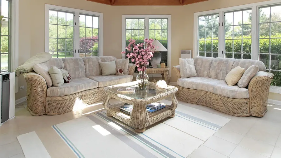 A bright sunroom with wicker furniture and a floral centerpiece.