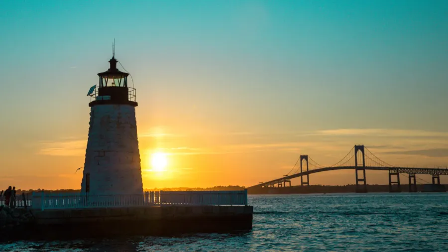 sunset over newport harbor lighthouse with bridge and colorful sky