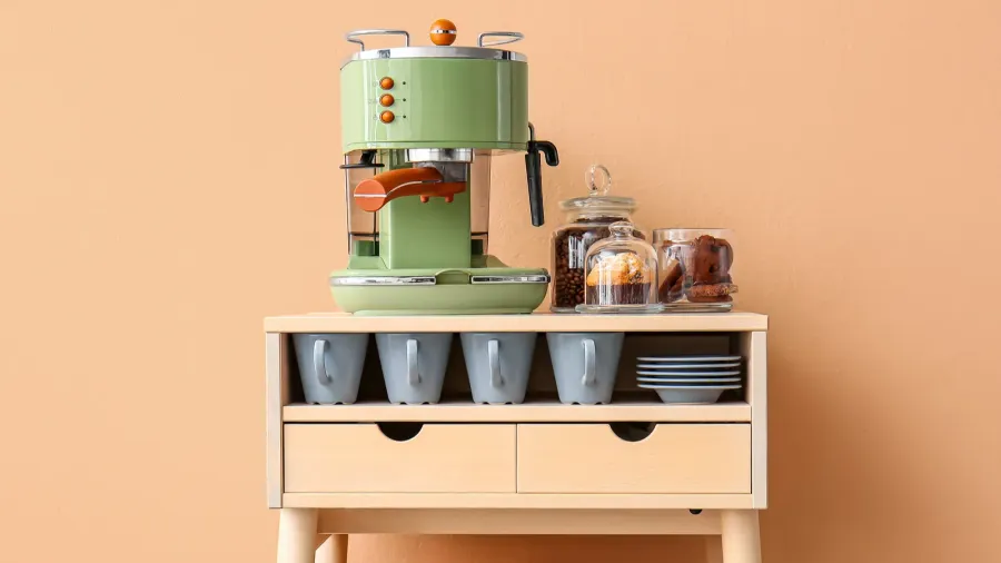 table with coffee machine snacks and cups near beige wall