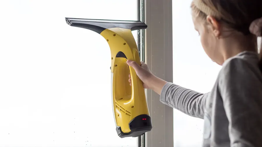 toddler girl washing big window in living room with portable