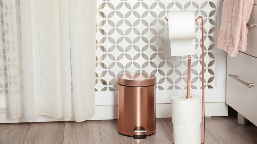 A metallic toilet paper holder with rolls and trash can in a bathroom.