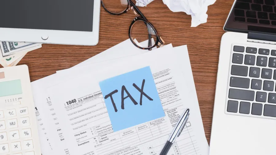Tax forms, digital devices, and a blue card from a top-down perspective.