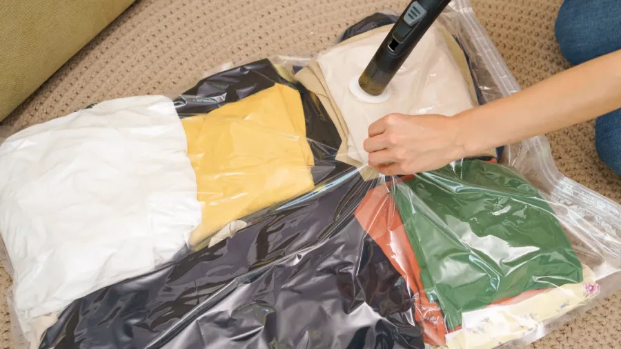 A woman vacuum sealing a transparent vacuum bag with winter clothing in it.