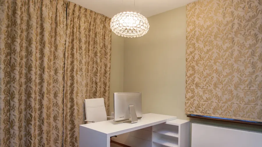 A luxurious home office interior with white desk and chair, printed drapes, and sculptural ceiling light.