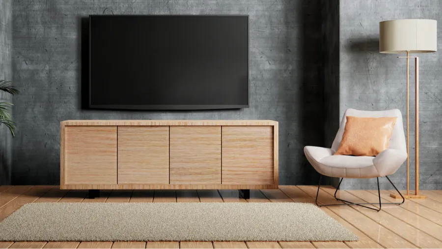 A living room with a large flat-screen TV mounted on a concrete wall, above a wooden TV stand and a chair.