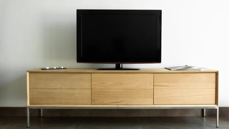 A TV on a wooden media console with storage drawers in front of a white wall.