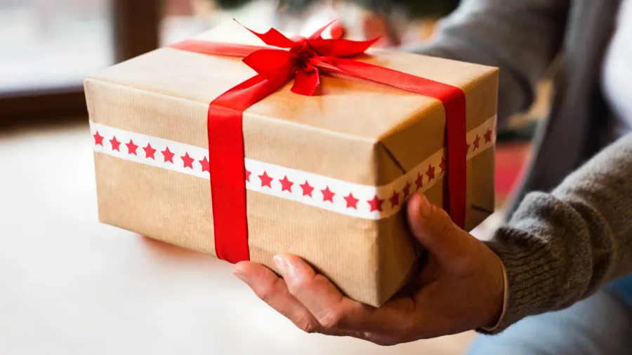 A woman holding present wrapped in a khaki paper and red ribbon.