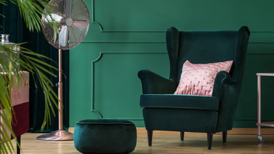 A living room interior with a bottle green velvet armchair with pink velvet cushion and a pouf.