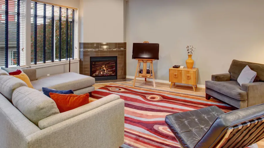 A stylish living room interior with a sofa, armchair, throw pillows, console table, fireplace, and an abstract rug.