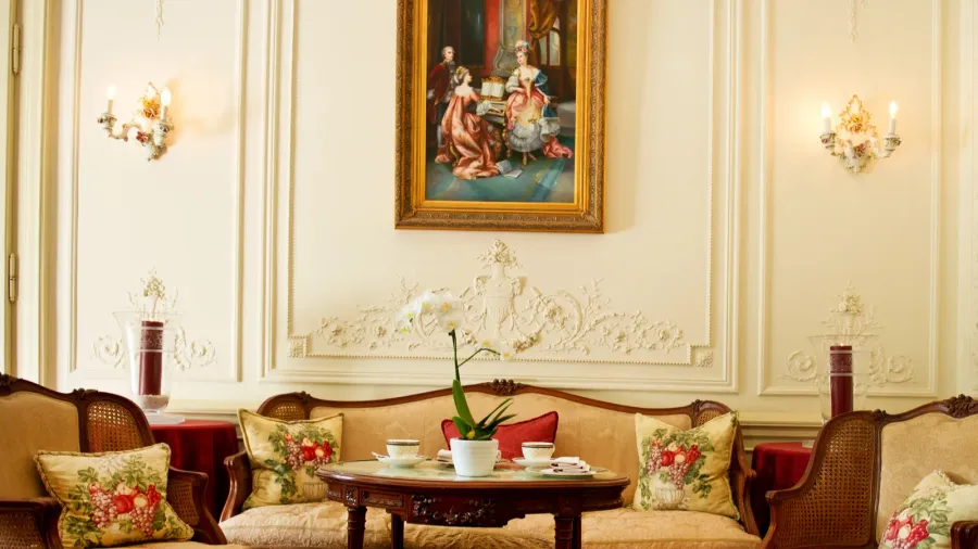 An opulent sitting room with an ornate painting, decorative cushions, and a table set for tea.