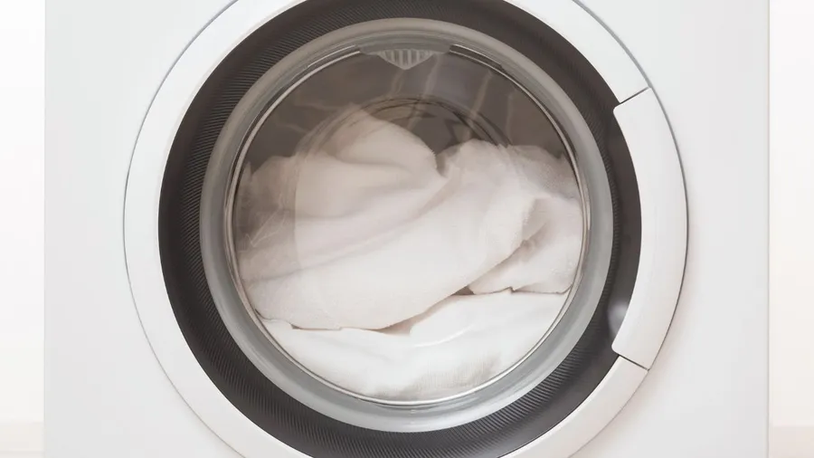 A front-loading washing machine with a white towel inside.