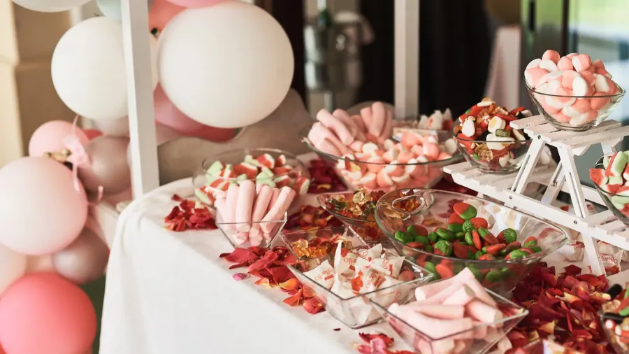 A dessert bar with different sweet treats, flower petals, and a balloon garland.
