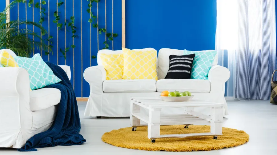 A stylish living room interior with cozy white sofas, throw blanket, throw pillows, and a wooden pallet coffee table with bottom shelf on a rug.