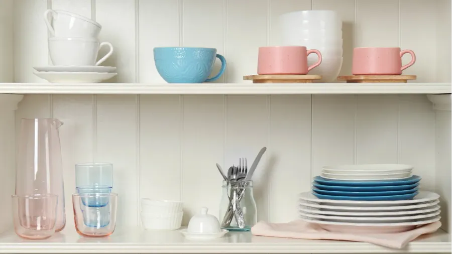 Shelves with stacked dishes, cups, and glasses in pastel colors.