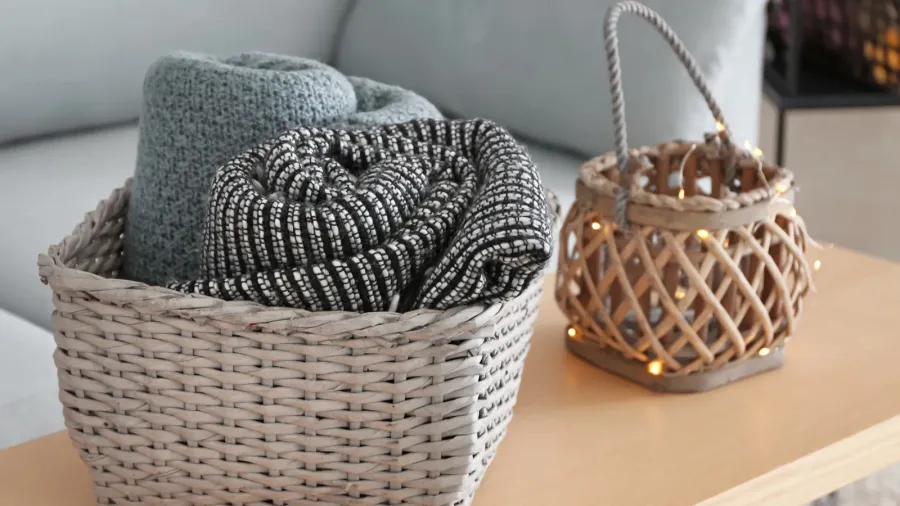 Wicker baskets on a wooden table with throw blankets and string lights.
