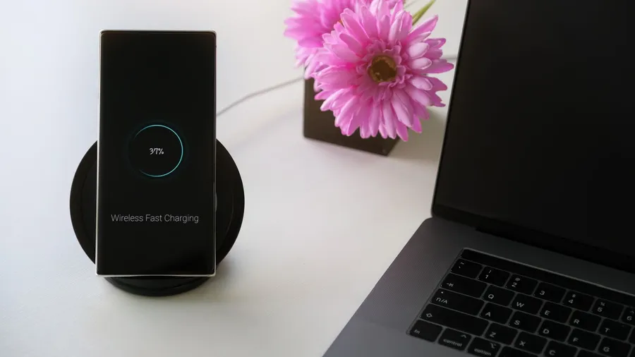 A mobile phone placed on a wireless charging pad with a laptop beside it.