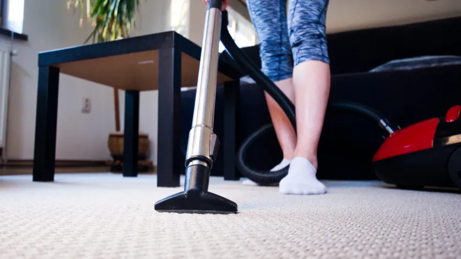 woman cleaning carpet with a vacuum cleaner in room