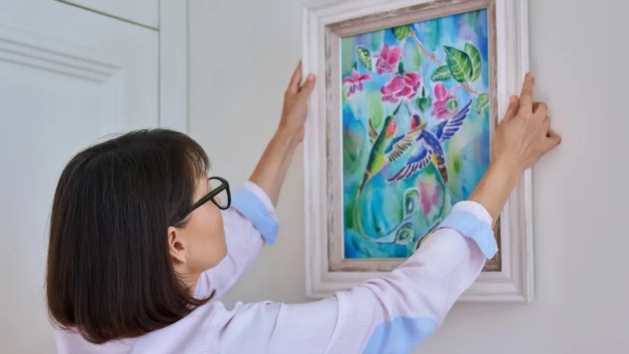 woman hanging floral birds art framed at home on the