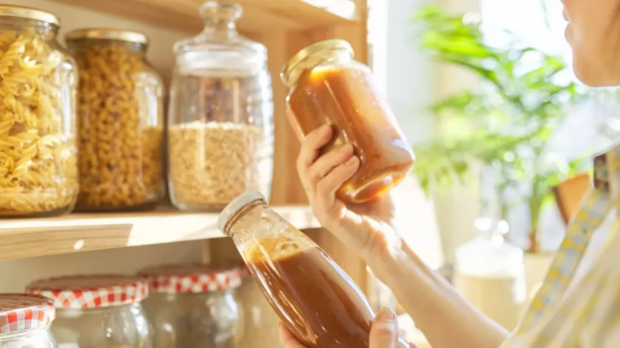 woman holding bottle with ketchup picking food from storage cabinet