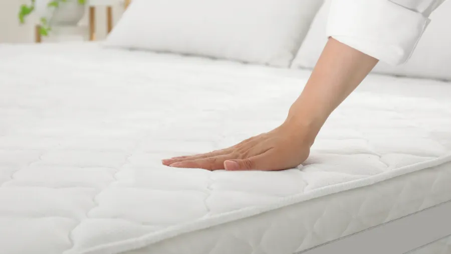 A woman touching soft white mattress on bed to check its firmness.