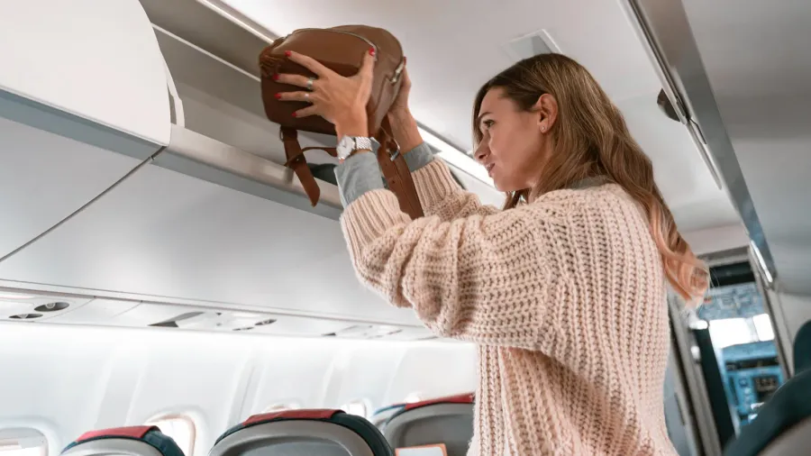 woman traveler putting luggage into overhead locker on airplane during