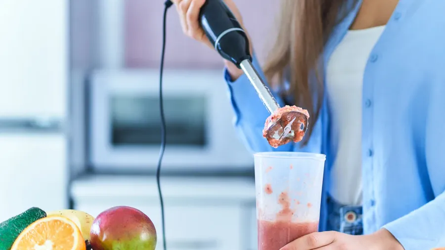 A woman using immersion blender to make smoothie.