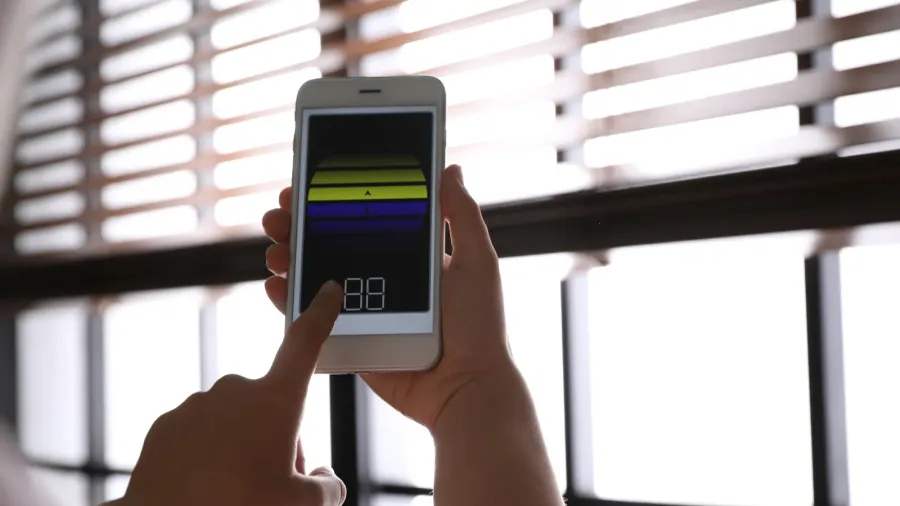 A woman using a smartphone to control the blinds on the windows.