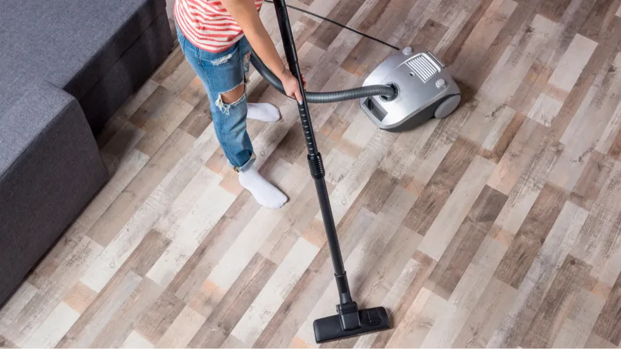 A person vacuuming a wooden floor with a vacuum cleaner.