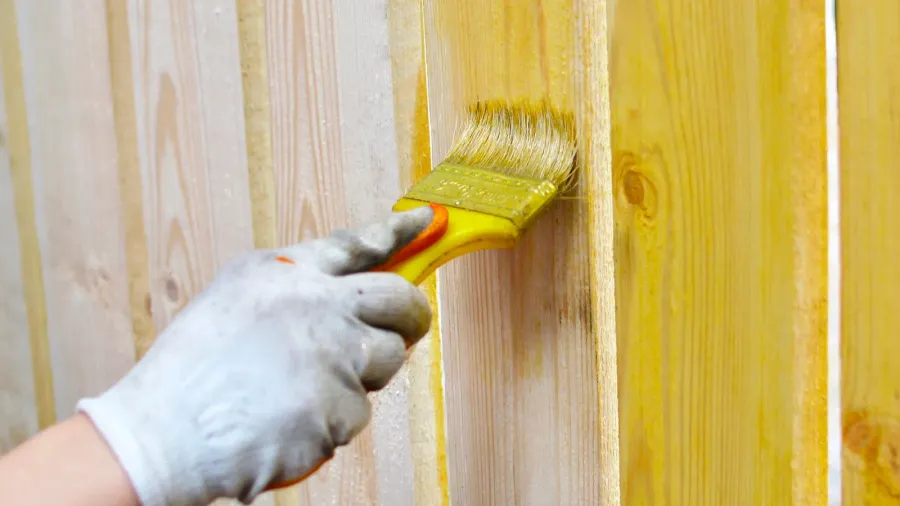 A person painting a wooden fence with yellow paint.