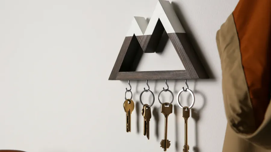 A modern key holder on a white wall with several keys hanging from it.