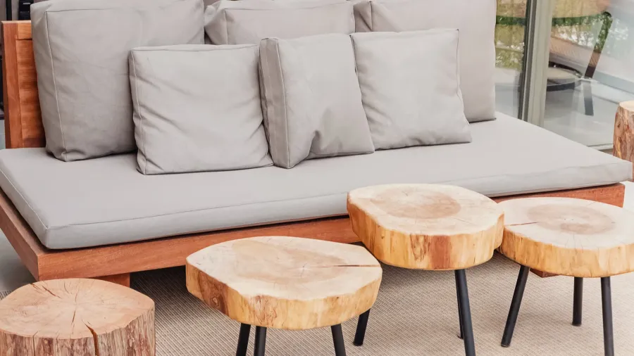 A stylish outdoor seating arrangement features a comfortable gray sofa with decorative pillows and uniquely crafted wooden stools.