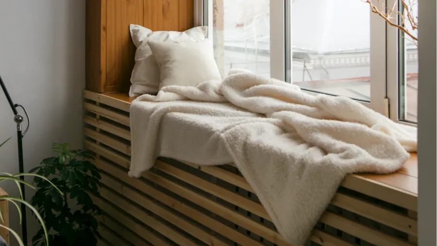 A cozy window seat with throw pillows and a soft, cozy throw blanket