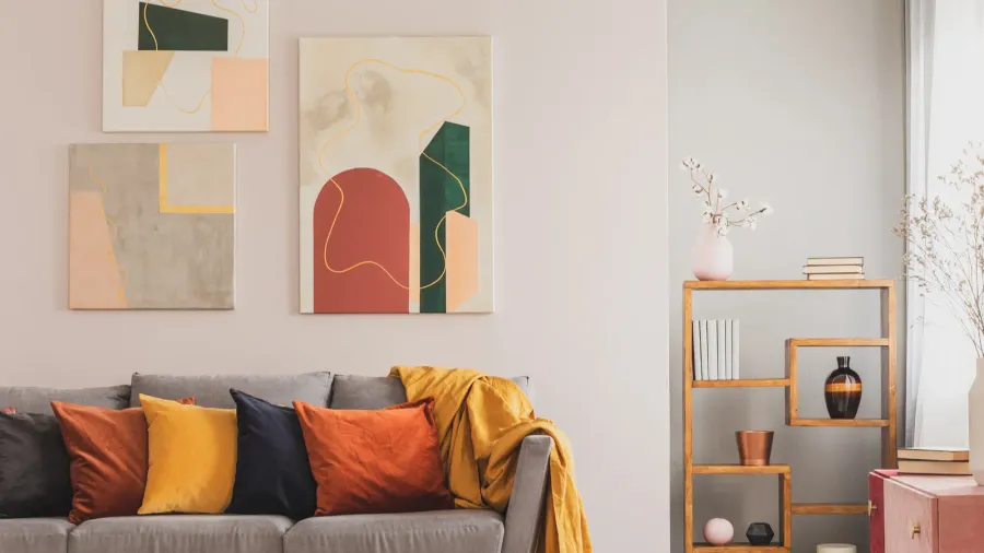 Colorful throw pillows on a gray sofa in front of a white wall with abstract artwork hanging on it.