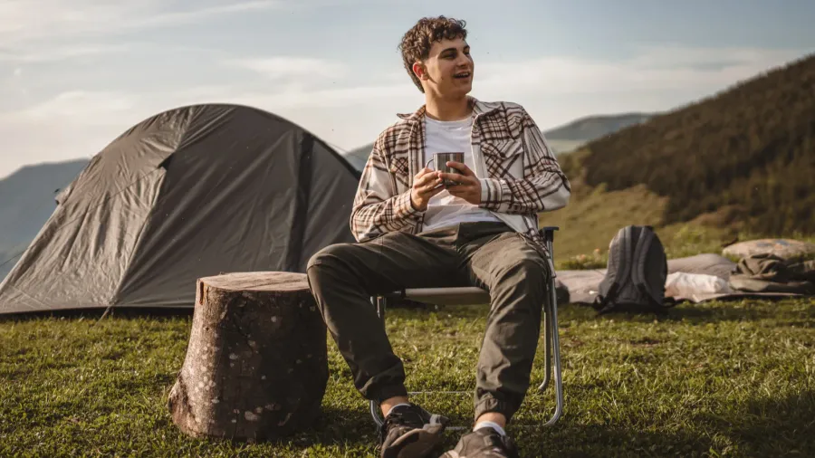 young boy sit in front tent and drink coffee on
