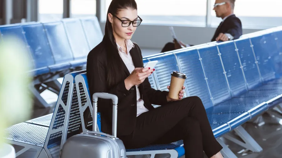 young businesswoman in glasses using smartphone in departure lounge at