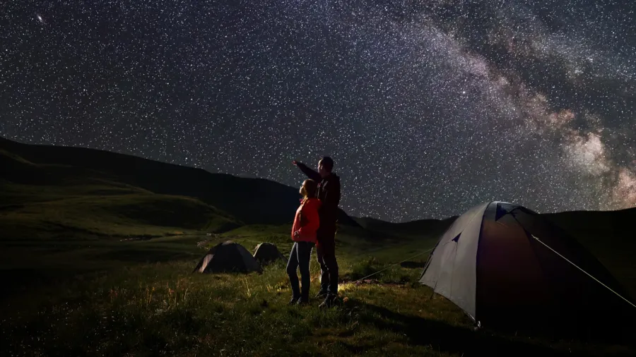 young couple hikers standing near tents at night camping under