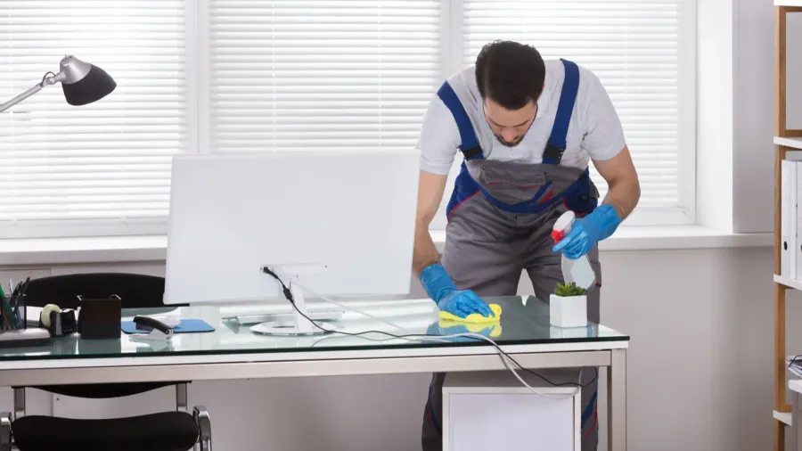 young male worker using spray for cleaning office desk